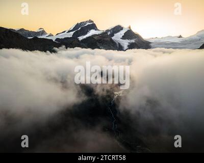 Un panorama di montagne innevate con alcune nuvole intorno, Alpi svizzere situate nel Vallese. Foto aerea scattata con un drone. Foto Stock