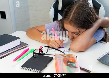 una ragazza a casa scrive pareggi, lezioni per un bambino a casa. stanchezza dovuta ai compiti. Lo studente è annoiato a fare i compiti. Foto Stock