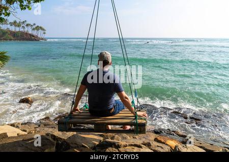 Mirissa, Sri Lanka - 13 dicembre 2023: Giovane su un altalena costruito da un pallet sulla spiaggia affacciata sul mare in Sri Lanka *** Junger Mann auf einer Schaukel gebaut aus einer Palette am Strand mit Blick auf das Meer in Sri Lanka Foto Stock