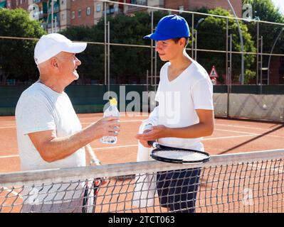 Nonno e nipote che parlano sul campo a giocare a tennis Foto Stock