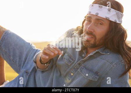 Uomo hippie con fascia fumante all'aperto Foto Stock