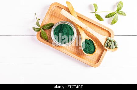 Un vasetto di vetro di polvere di spirulina organica verde e due cucchiai di legno riempiti di polvere e capsule su un vassoio di legno Vista dall'alto. Disintossicazione. Foto Stock