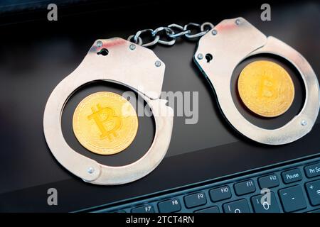 un bitcoin dorato sullo sfondo di manette e una tastiera nera per computer portatile. Divieto di vendita e acquisto di bitcoin e criptovalute. Foto Stock
