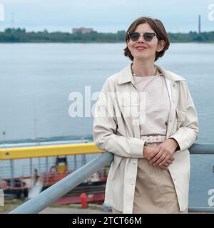 Una donna con un vestito bianco si trova su un ponte pedonale sullo sfondo del mare Foto Stock