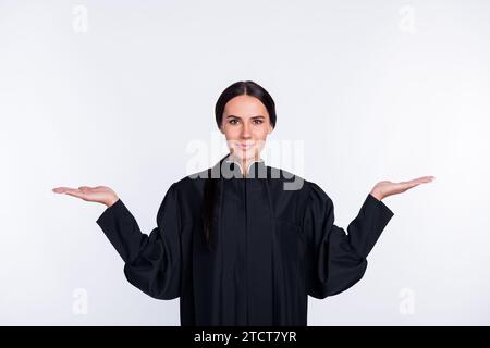 Foto di felice buon umore sorridente bella donna giudice tiene la mano in equilibrio isolato su sfondo di colore bianco Foto Stock