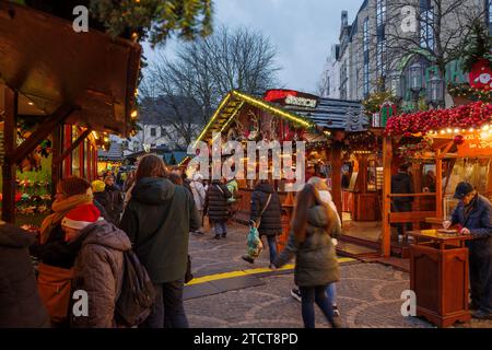 Bonn, Germania - 6 dicembre 2023: Scena al crepuscolo in un vivace mercatino di Natale con decorazioni natalizie e acquirenti che visitano le bancarelle delle feste. Foto Stock