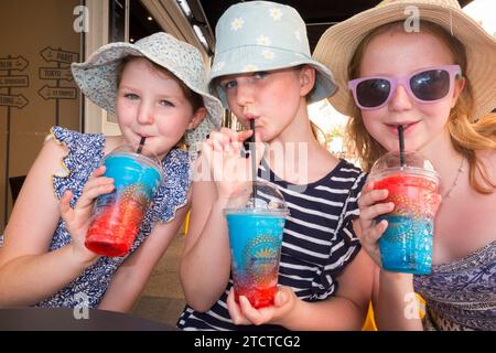 Tre ragazze bevono slushi fresco fresco, ghiacciato o gelato, una marca rinfrescante di ghiaccio liquido. Vengono bevute attraverso la paglia da tre bambini/bambini. (135) Foto Stock