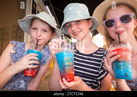 Tre ragazze bevono slushi fresco fresco, ghiacciato o gelato, una marca rinfrescante di ghiaccio liquido. Vengono bevute attraverso la paglia da tre bambini/bambini. (135) Foto Stock