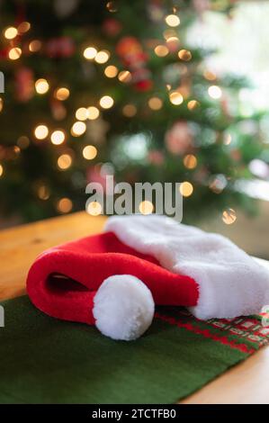 Un cappello di Babbo Natale su un tavolino di pino con un albero di Natale sullo sfondo. Foto Stock