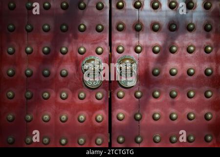 Tradizionali porte cinesi in legno rosso con battitori in ottone e borchie ornamentali. Foto Stock