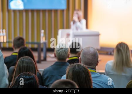 Vista posteriore dei colleghi di lavoro che ascoltano una oratrice sul palco della sala conferenze Foto Stock