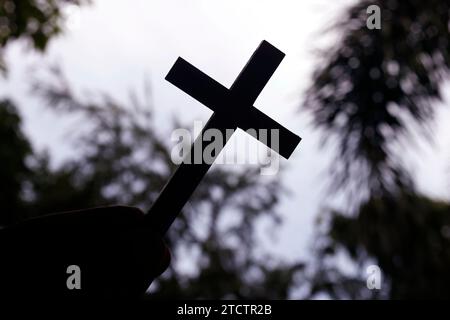 Uomo che tiene una croce cristiana contro il cielo. Simbolo religioso del cristianesimo. Foto Stock