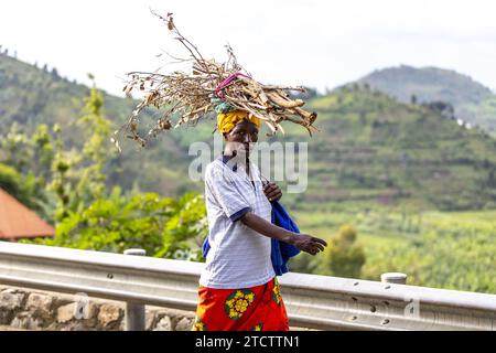 Uomo che cammina lungo una strada con un fascio di ramoscelli sulla testa nel Ruanda occidentale Foto Stock