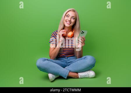 Foto integrale di una ragazza che sogna che naviga sulle cuffie preferite per playlist dello smartphone dell'app spotify isolate su sfondo verde Foto Stock