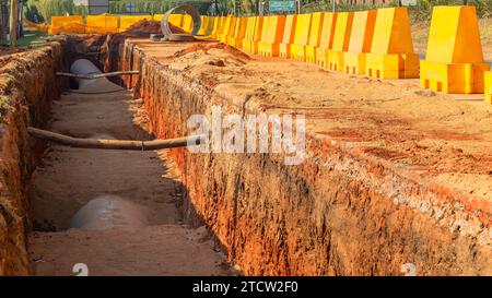 Costruzione di un nuovo layout di tubi dell'acqua in acciaio lavori di terra sotterranei scavi di trincea da vicino con vista sul progetto ingegneristico. Strada di campagna con yello Foto Stock