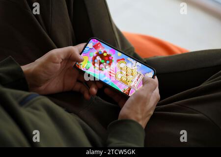 Candy Crush Saga gioco per dispositivi mobili iOS su schermo dello smartphone iPhone 15 in mani maschili durante l'azione di gioco mobile. Giochi e intrattenimento mobili su dispositivi portatili Foto Stock