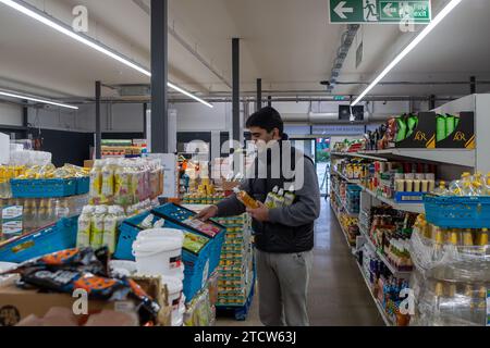 Slough, Regno Unito. 14 dicembre 2023. Volontario Deedar al lavoro. Notjust A Store ha aperto un nuovo grande negozio al Westgate Retail Park sulla A4 a Slough, Berkshire, accanto a Currys. L'enorme negozio vende cibo a prezzi scontati, dove i clienti possono riempire un cestino con articoli a £5 che costerebbero circa £15 altrove. Gran parte del cibo è passato il migliore prima della data o è in eccesso, ma è comunque perfettamente accettabile da consumare. È aperto a tutti coloro che odiano gli sprechi e amano fare affari. Gli acquirenti non devono essere membri per fare acquisti in negozio o avere una soglia di reddito. Credito: Maureen McLean/Alamy Live ne Foto Stock