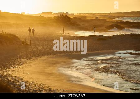 Persone che camminano al tramonto lungo la riva della spiaggia di Ses Platgetes a es Caló (Formentera, Isole Pityusic, Isole Baleari, Mar Mediterraneo, Spagna Foto Stock