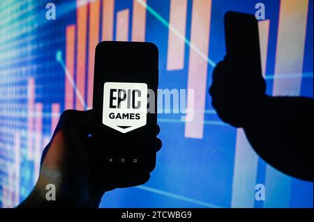 In questa foto, sullo smartphone viene visualizzato il logo Epic Games con le percentuali del mercato azionario sullo sfondo. Foto Stock