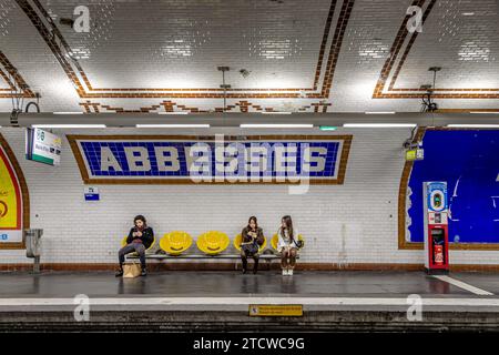 Gente seduta in attesa di un treno alla stazione della metropolitana di Abbesses nel 18° arrondissement di Parigi, Francia Foto Stock