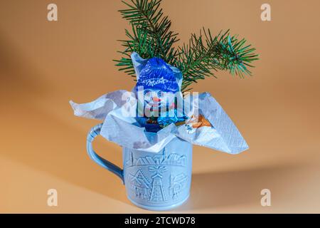 Splendida vista del pupazzo di neve al cioccolato in regalo di Natale nascosto in una tazza isolata su sfondo rosso. Foto Stock