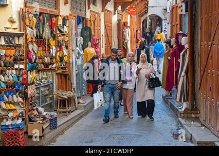 I marocchini camminano lungo la strada dello shopping, accanto al negozio di scarpe e al negozio di abbigliamento a medina, nella città di FES/Fez, Fez-Meknes, Marocco Foto Stock