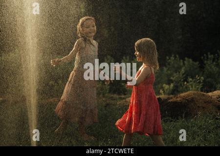 Le ragazze giocano in giardino in estate, spruzzano d'acqua, si divertono. Foto Stock