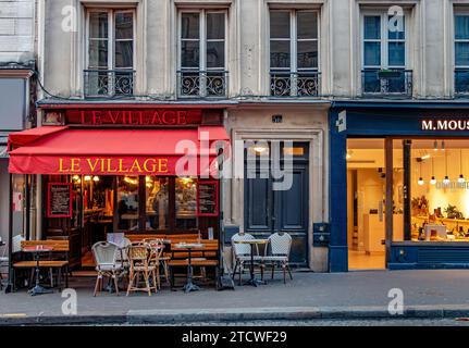 Tavoli e sedie fuori le Village, un piccolo ristorante, caffetteria in Rue des Abbesses, Montmartre nel 18° arrondissement di Parigi, Francia Foto Stock
