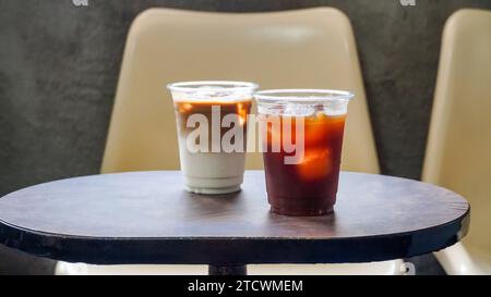 Ghiaccio americano e caffè a base di latte sul tavolo. Due tazze di plastica da asporto di caffè americano freddo e latte freddo su tavolo in legno. Foto Stock