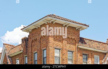 Gronde profonde e tetto in tegole completano la torre angolare quadrata della 32-65 80th Street, un basso edificio di appartamenti in mattoni con negozi a Jackson Heights. Foto Stock