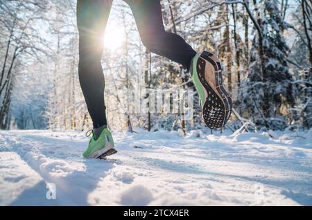 Suola da running immagine ravvicinata dei piedi da jogger invernali nelle sneakers da running sul sentiero innevato del parco durante la giornata di sole. Immagine della suola per la visione posteriore. Foto Stock