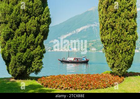 Bellagio Italia - 8 maggio 2011; gruppi turistici che attraversano il lago di Como in una pittoresca barca d'epoca, passando tra cipressi e un giardino. Foto Stock