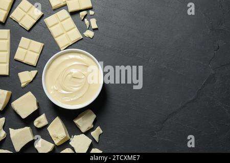 Gustosa pasta di cioccolato bianco in ciotola e pezzi su tavolo nero, piatto. Spazio per il testo Foto Stock