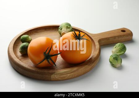 Tagliere con cavoletti di Bruxelles e pomodori su tavola di legno bianco Foto Stock