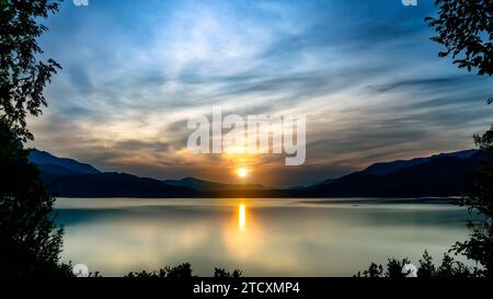 vista del lago all'alba, è possibile vedere le montagne e le foglie degli alberi che formano una cornice Foto Stock