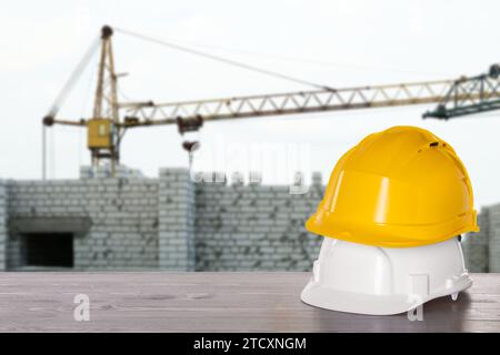 Attrezzatura di sicurezza. Cappelli rigidi su superfici in legno vicino al cantiere con gru a torre all'aperto, spazio per testo Foto Stock