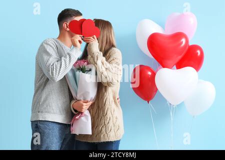 Coppia incantevole con bouquet di fiori, cuori di carta e palloncini a forma di cuore su sfondo blu. Festa di San Valentino Foto Stock