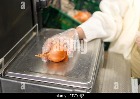 Vista ravvicinata di una giovane donna irriconoscibile che mette una cipolla al peso in una bilancia self-service Foto Stock