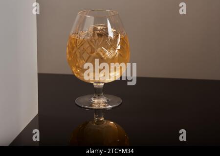 Bicchiere di brandy, cognac con ghiaccio su una superficie fredda riflettente. Foto Stock