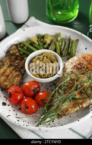 Pollo gustoso, verdure con dragoncello e pesto serviti al tavolo, primo piano Foto Stock