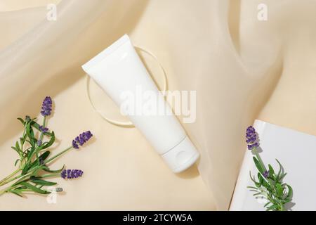 Primo piano di fiori di lavanda freschi e un tubo di cosmetici senza marchio su uno sfondo di tessuto beige. L'uso di olio essenziale di lavanda sulla pelle si scatena Foto Stock
