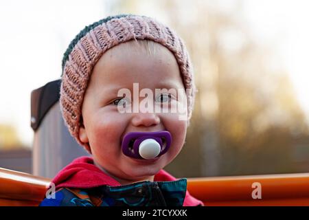 Umea, Svezia - 3 ottobre 2023: Bambino felice con succhietto in bocca e berretto a maglia casalinga Foto Stock
