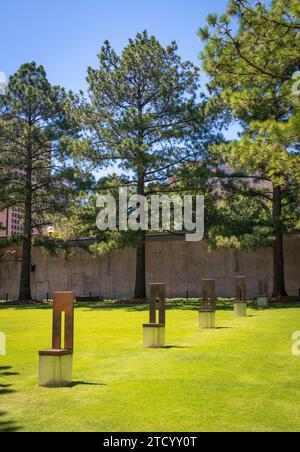File di sculture di sedie in bronzo e vetro si ergono su un prato verde con alti pini sullo sfondo al Oklahoma City National Memorial, Oklahoma. Foto Stock