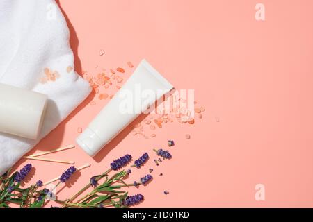 Un tubo bianco su sfondo rosa con sale rosa himalayano, fiori di lavanda, candele profumate, fiammiferi e un asciugamano di cotone. Etichette vuote per il branding. Foto Stock