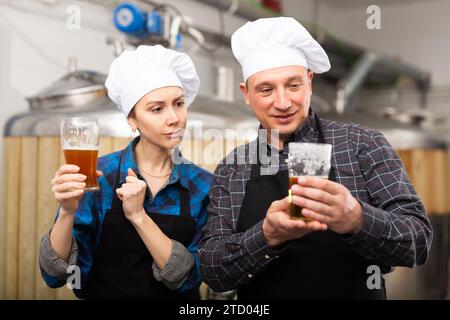 I produttori di birra interessati, maschi e femmine, che esaminano la qualità della birra in birrificio Foto Stock