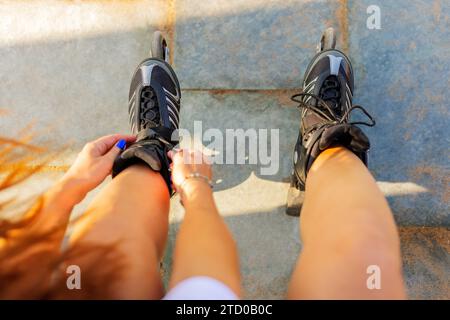 Ritaglio ad angolo elevato di donna anonima che lega pizzi di pattini a rotelle neri in linea sul sentiero nel parco Foto Stock
