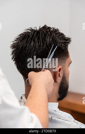 Tagliate le mani di una parrucchiera femminile irriconoscibili tagliando i capelli di un cliente maschio con le forbici al salone Foto Stock