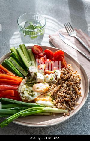 Una colazione nutriente che presenta un pasto equilibrato con verdure fresche, feta cremosa, grano saraceno ricco di proteine e uova fritte al pesto. Foto Stock