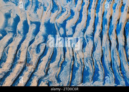 Arte astratta e naturale di motivi ondulati di sabbia evidenziati da ombre blu profonde, che mostrano texture e forme create dalla luce e dall'ombra. Foto Stock