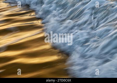 Una cattura astratta delle onde oceaniche con un gioco di luce solare dorata che si riflette sulla superficie dell'acqua, creando un bellissimo contrasto con le sfumature blu Foto Stock